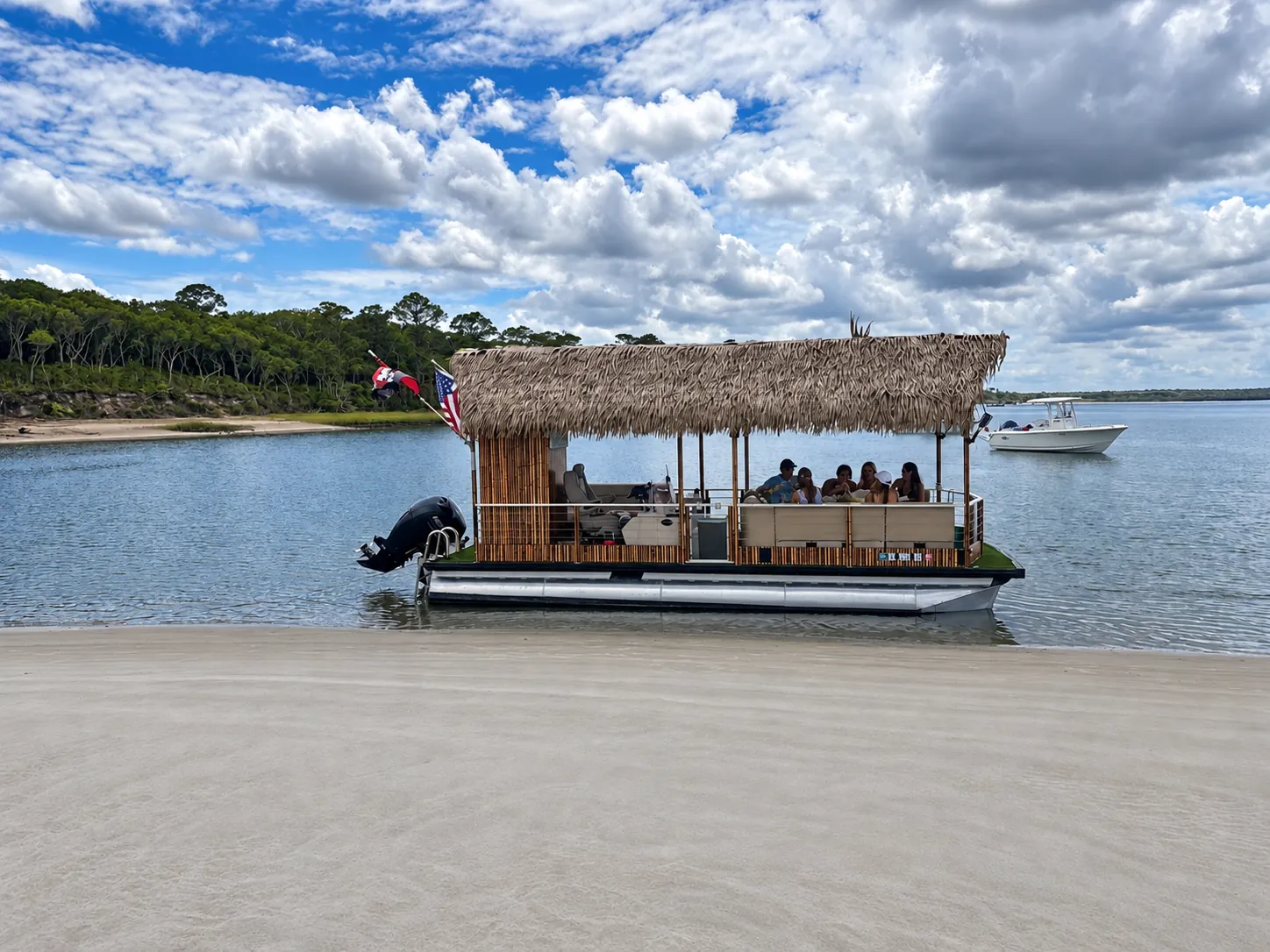 Tiki hut party boat anchored at a sandbar beach with guests on board